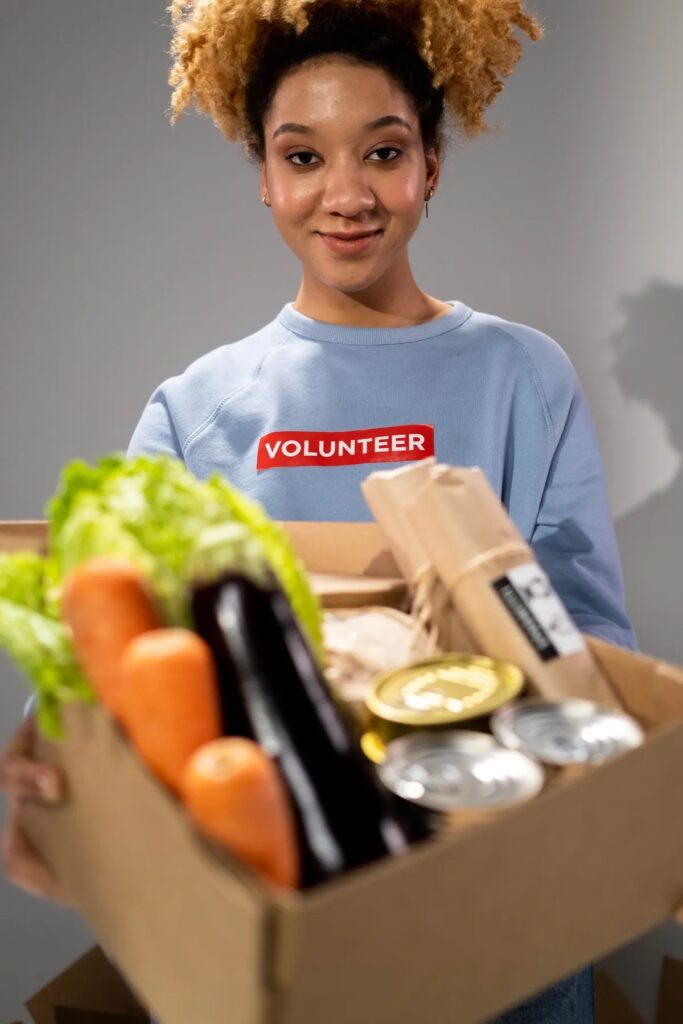 A volunteer holding a box of fresh vegetables and pantry staples for a weekly grocery delivery